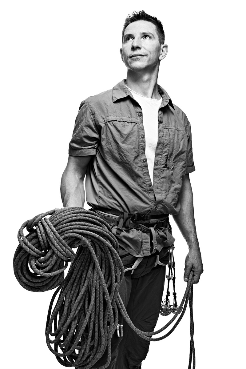 Black and white studio portrait of Duncan looking up, a coiled climbing rope over his arm.